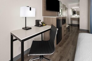 A hotel room with a desk, chair, television, and a bed.