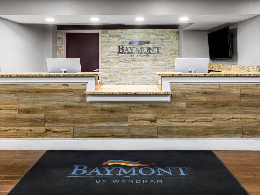 A reception desk with a stone wall backdrop and a black mat with 'Baymont by Wyndham' branding.
