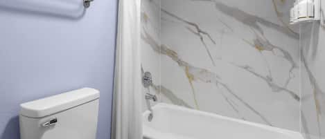 A bathroom with a toilet, a shower with a marble wall, and a towel rack.