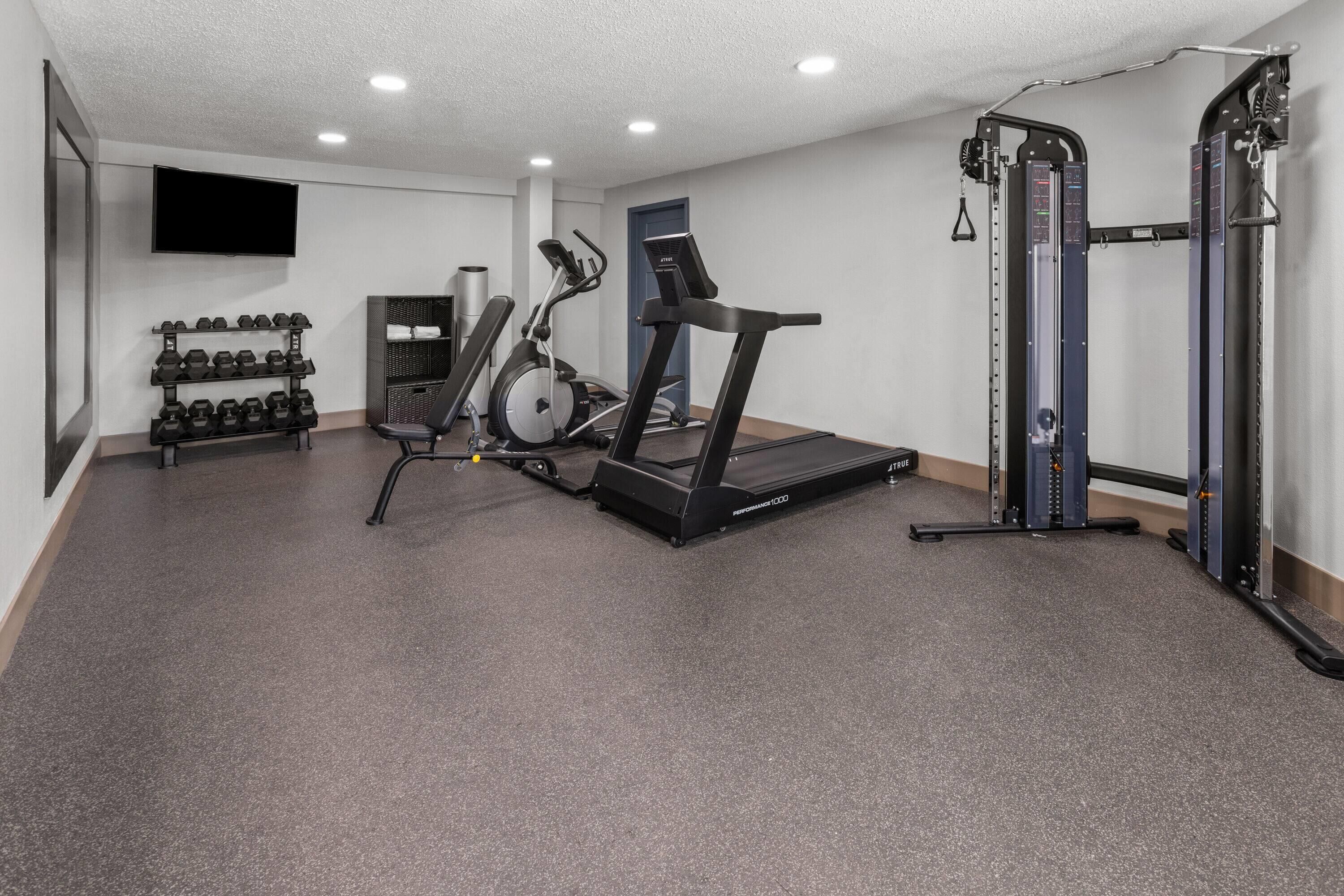 Un gimnasio con cinta de correr, elíptica, banco de pesas y mancuernas.