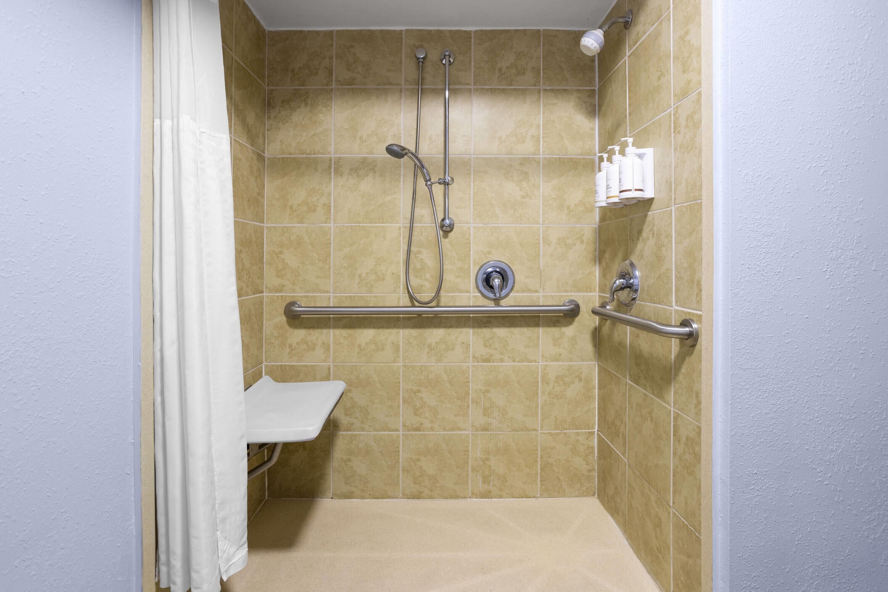 A shower with a grab bar, a handheld showerhead, and a handheld faucet.