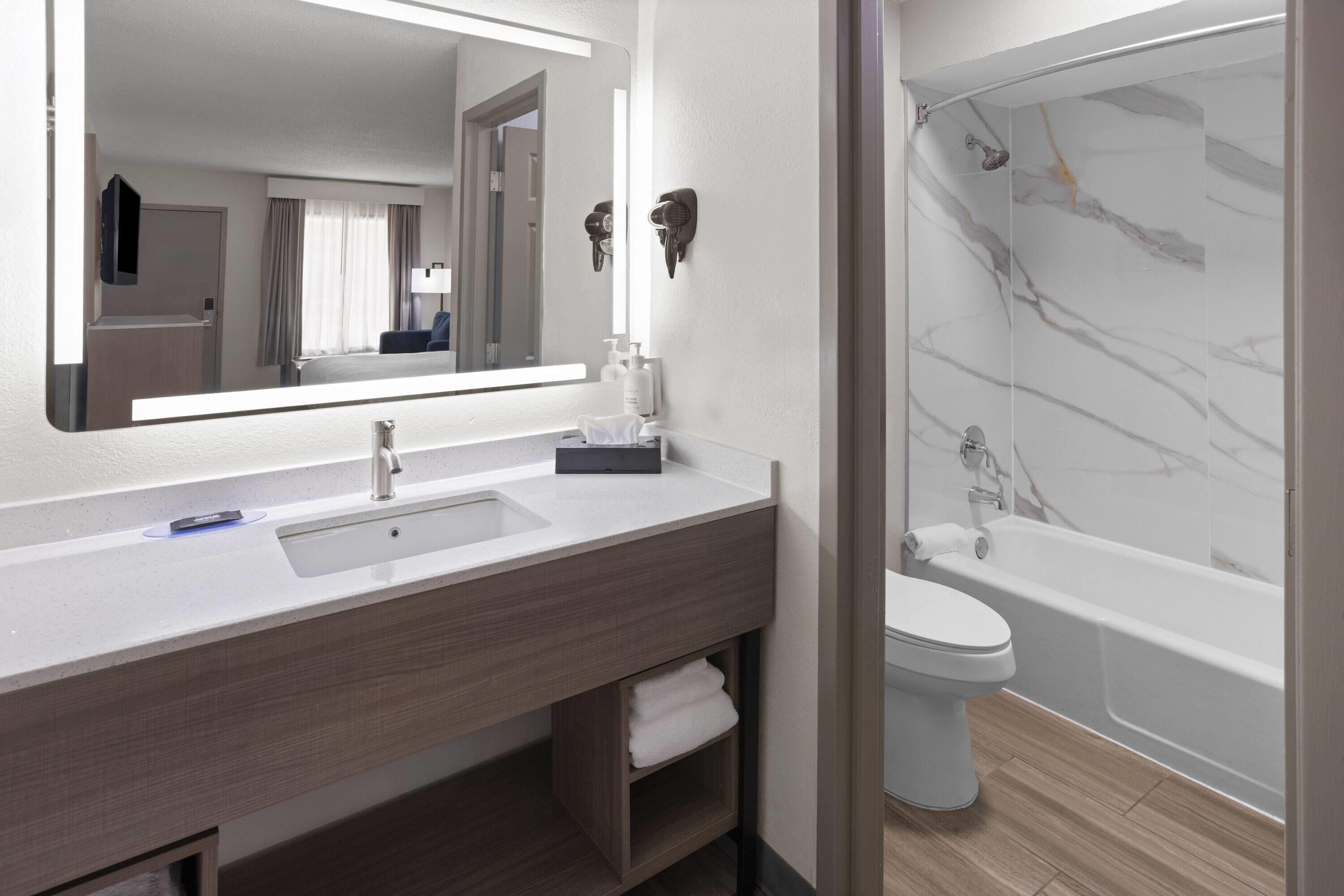 A modern bathroom with a large mirror, a sink, a toilet, and a shower.