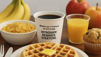 A breakfast setting with waffles, a muffin, a bowl of cereal, a cup of coffee, and a glass of orange juice.