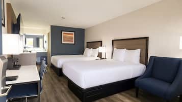 A hotel room with two beds, a desk, a chair, and a bathroom visible in the background.