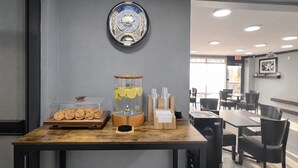 A cafe counter with a clock, a glass jar with lemon slices, and a tray of cookies.