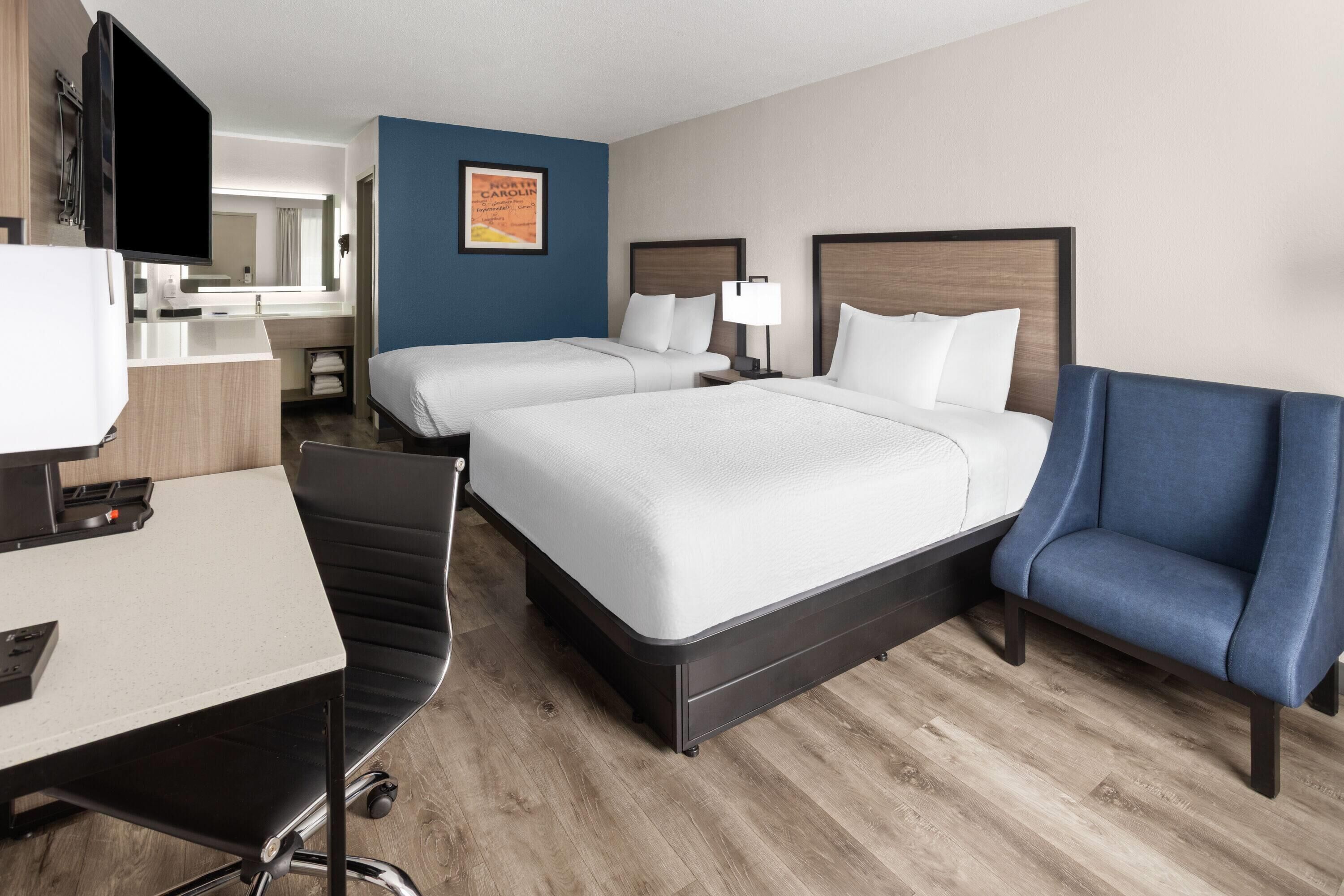 A hotel room with two beds, a desk, a chair, a TV, and a bathroom.