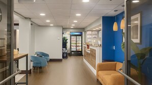 A modern interior with a reception desk, a seating area with chairs, and a refrigerator stocked with beverages.