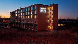 Un hotel moderno con un letrero que dice "Four Points by Sheraton". Cuenta con un edificio rectangular con múltiples ventanas y una entrada destacada.