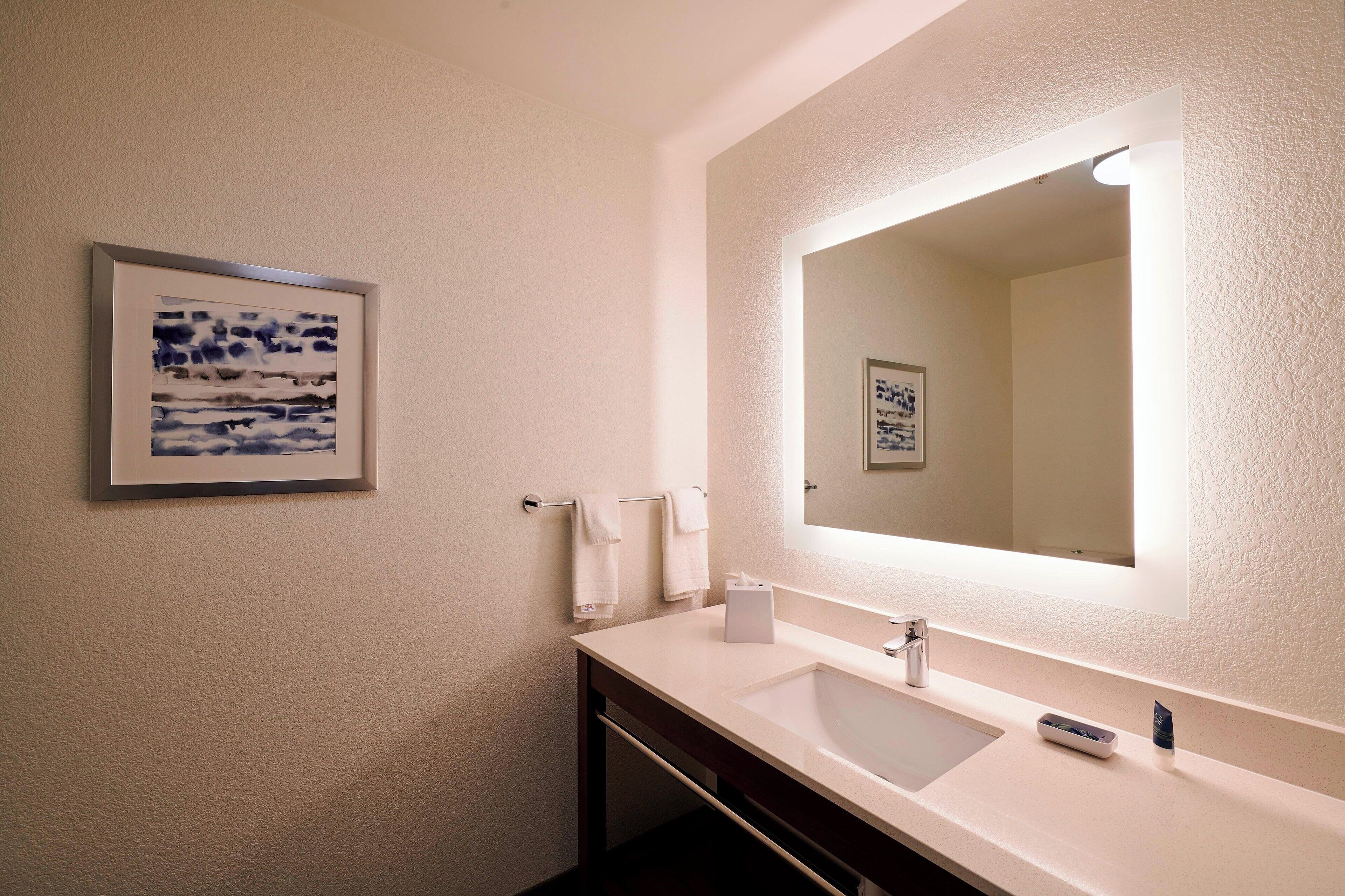 Une salle de bain avec un lavabo blanc, un grand miroir et une œuvre d’art encadrée accrochée au mur.