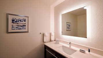 Une salle de bain avec un lavabo blanc, un grand miroir et une œuvre d’art encadrée accrochée au mur.