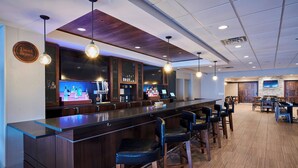 Una zona de bar con una barra larga, varios taburetes y una pantalla de televisión.