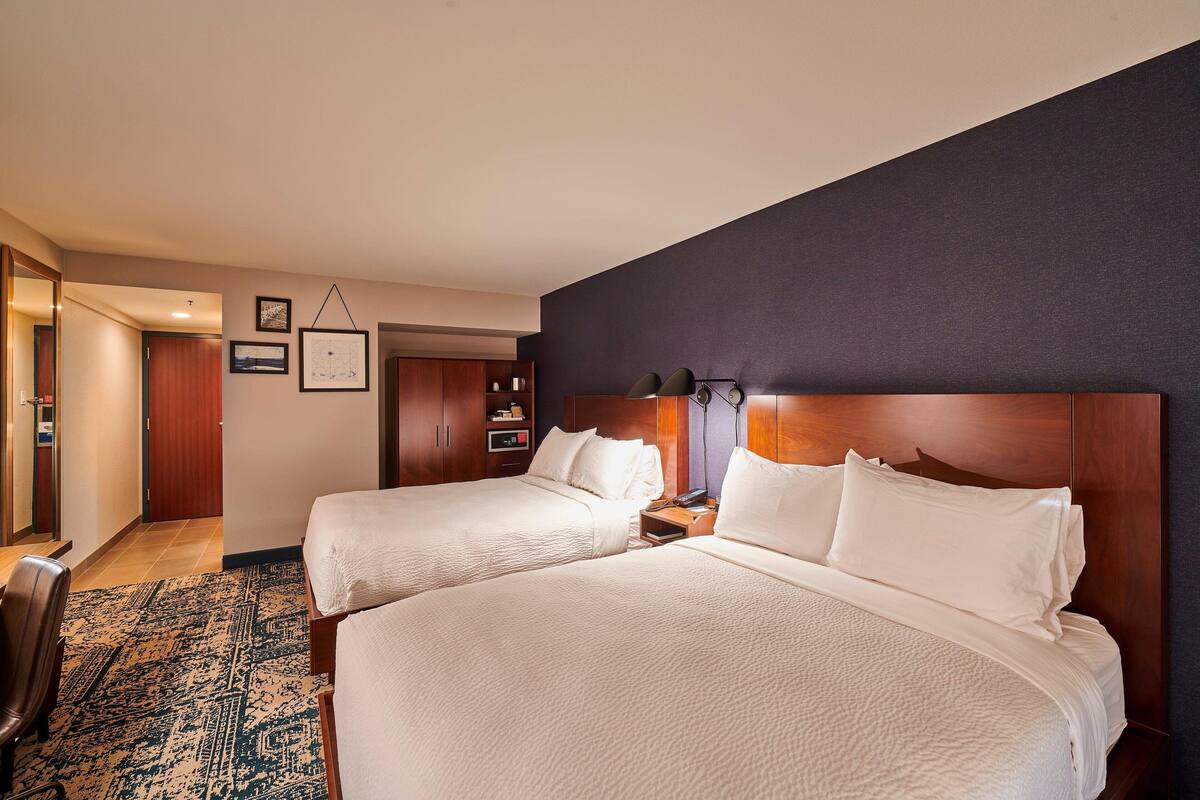 A hotel room with two beds, a desk, a chair, and a large window.