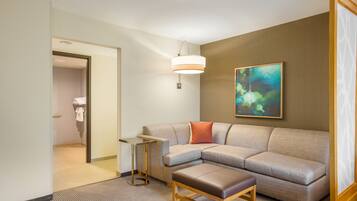 Una habitación de hotel moderna con un sofá modular, una mesita auxiliar pequeña, una lámpara colgante y un cuadro en la pared.
