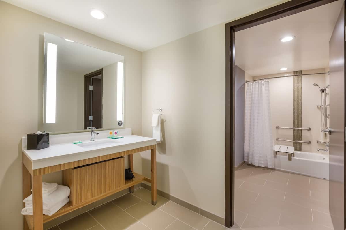 A modern bathroom with a large mirror, two sinks, a wooden vanity, a towel rack, and a shower area with a glass door.