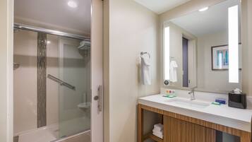 Une salle de bain moderne avec une douche à parois de verre, un lavabo blanc avec un grand miroir et des meubles en bois.