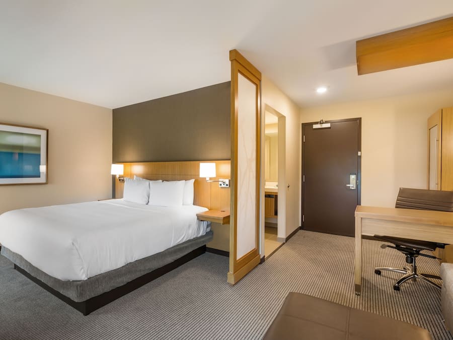 A hotel room with a large bed, bedside tables, a desk, and a mirror.