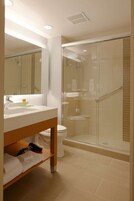 Un baño moderno con ducha de vidrio, un lavamanos blanco y un espejo encima.