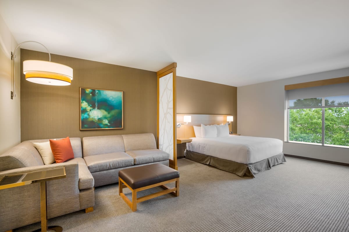 A hotel room with a sofa, a small table, a bed, and a large window.