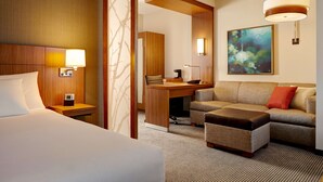 Una habitación de hotel con cama, escritorio, sofá y un cuadro en la pared.