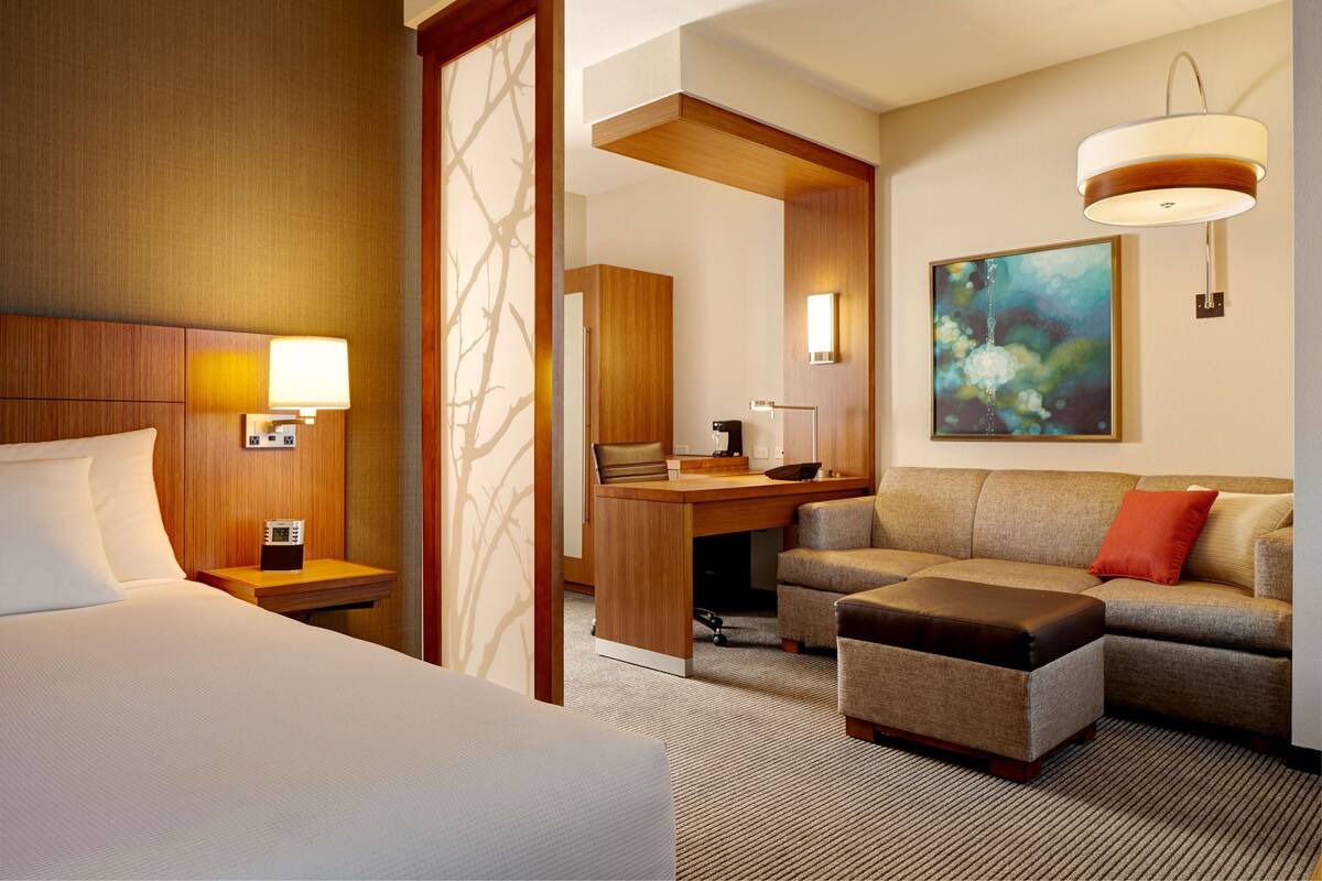 A hotel room with a bed, a desk, a sofa, and a painting on the wall.