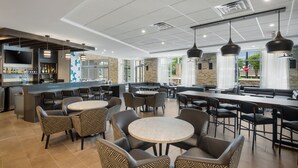Un restaurante moderno con una zona de bar, diversas opciones de asientos, incluidas mesas redondas y cabinas, y vistas al exterior a través de amplios ventanales.