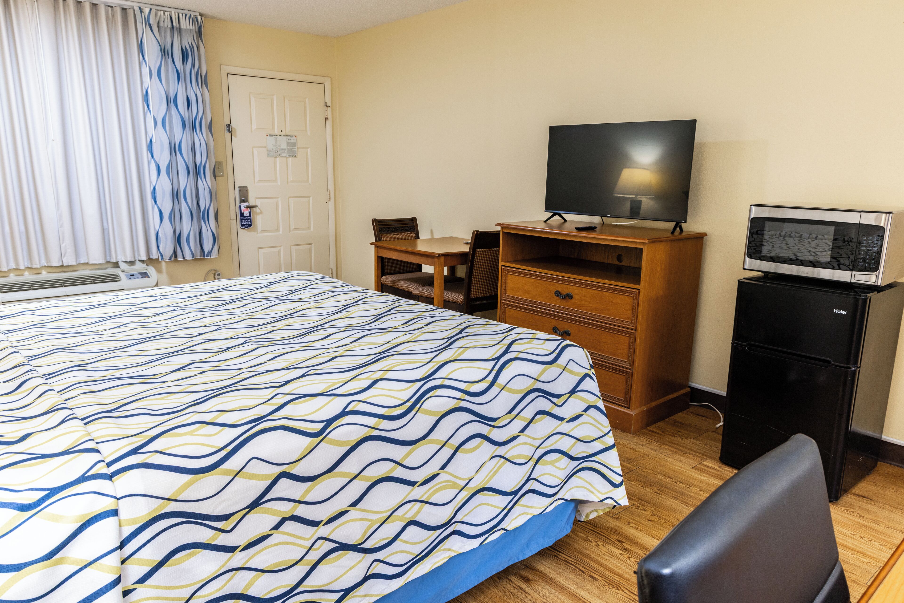 A hotel room with a bed, a desk with a television, a microwave, and a chair.