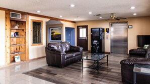 A spacious living area with a leather sofa, a glass coffee table, and a wooden bookshelf. - Boerne Inn and Suites (Boerne)