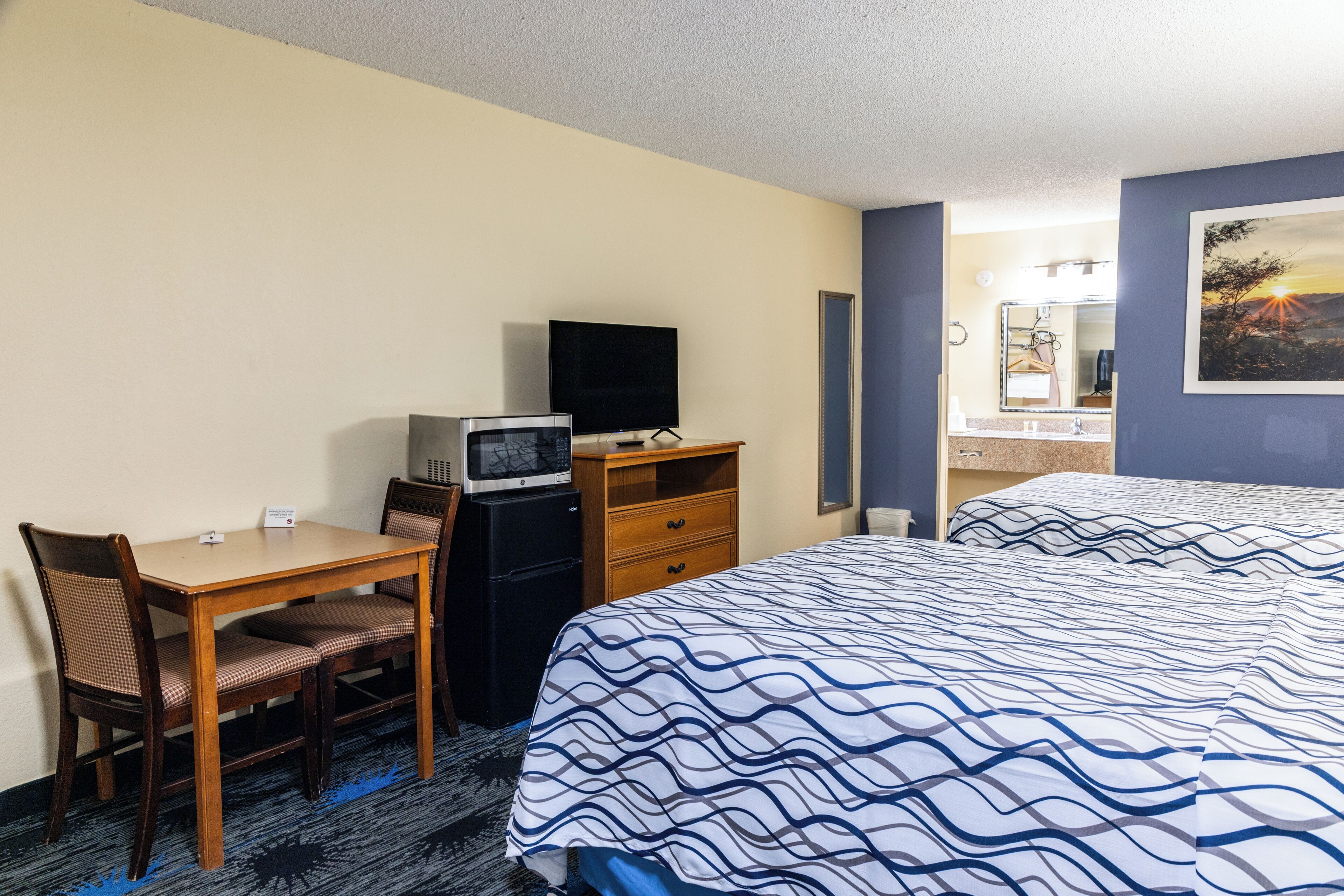 Une chambre d’hôtel comprenant un lit, un bureau avec une télévision, un four à micro-ondes et une commode.