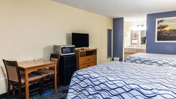 Une chambre d’hôtel comprenant un lit, un bureau avec une télévision, un four à micro-ondes et une commode.