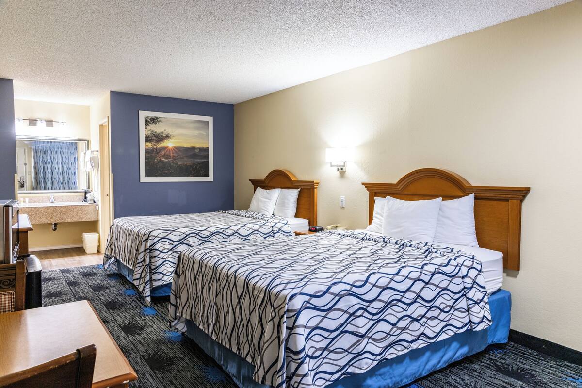 A hotel room with two beds, a bathroom, and a desk.