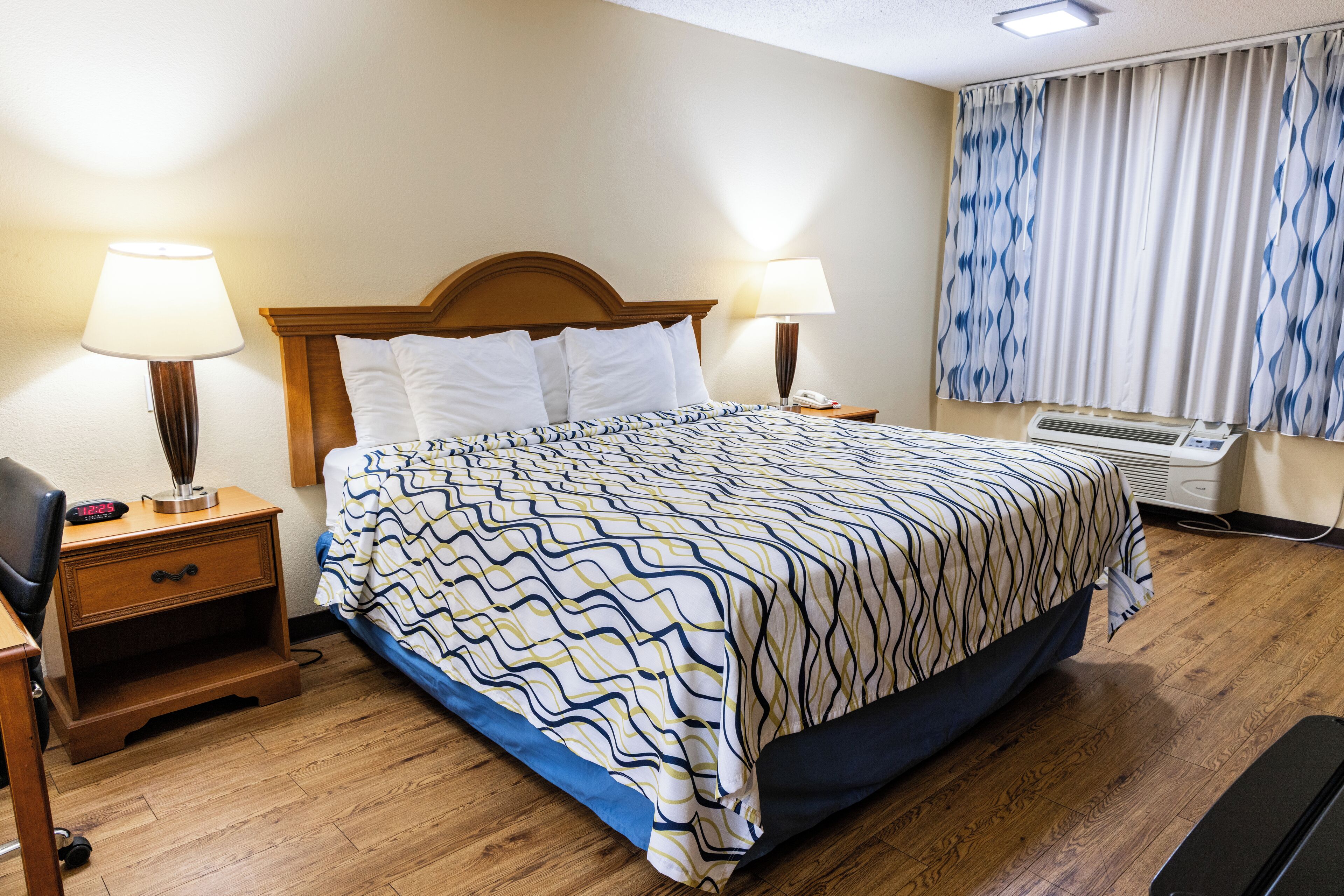 A hotel room with a wooden bed, two bedside tables, a lamp, a telephone, and a window with curtains.