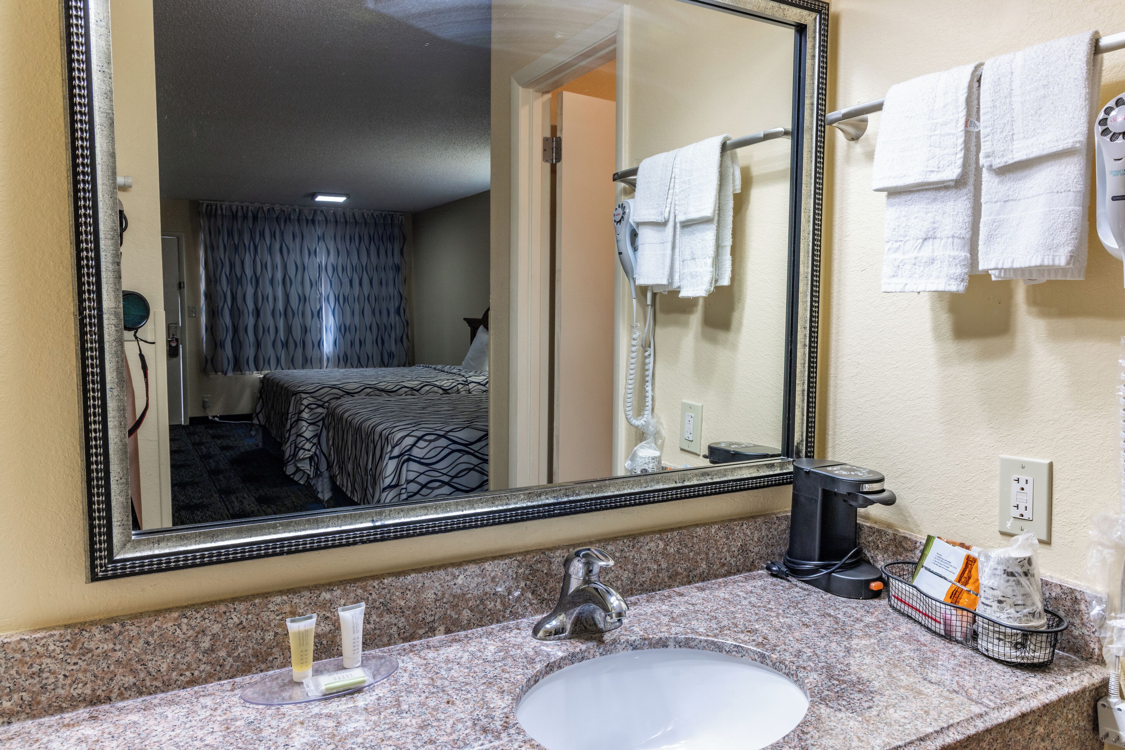 A hotel bathroom with a large mirror, a sink, and a hairdryer.