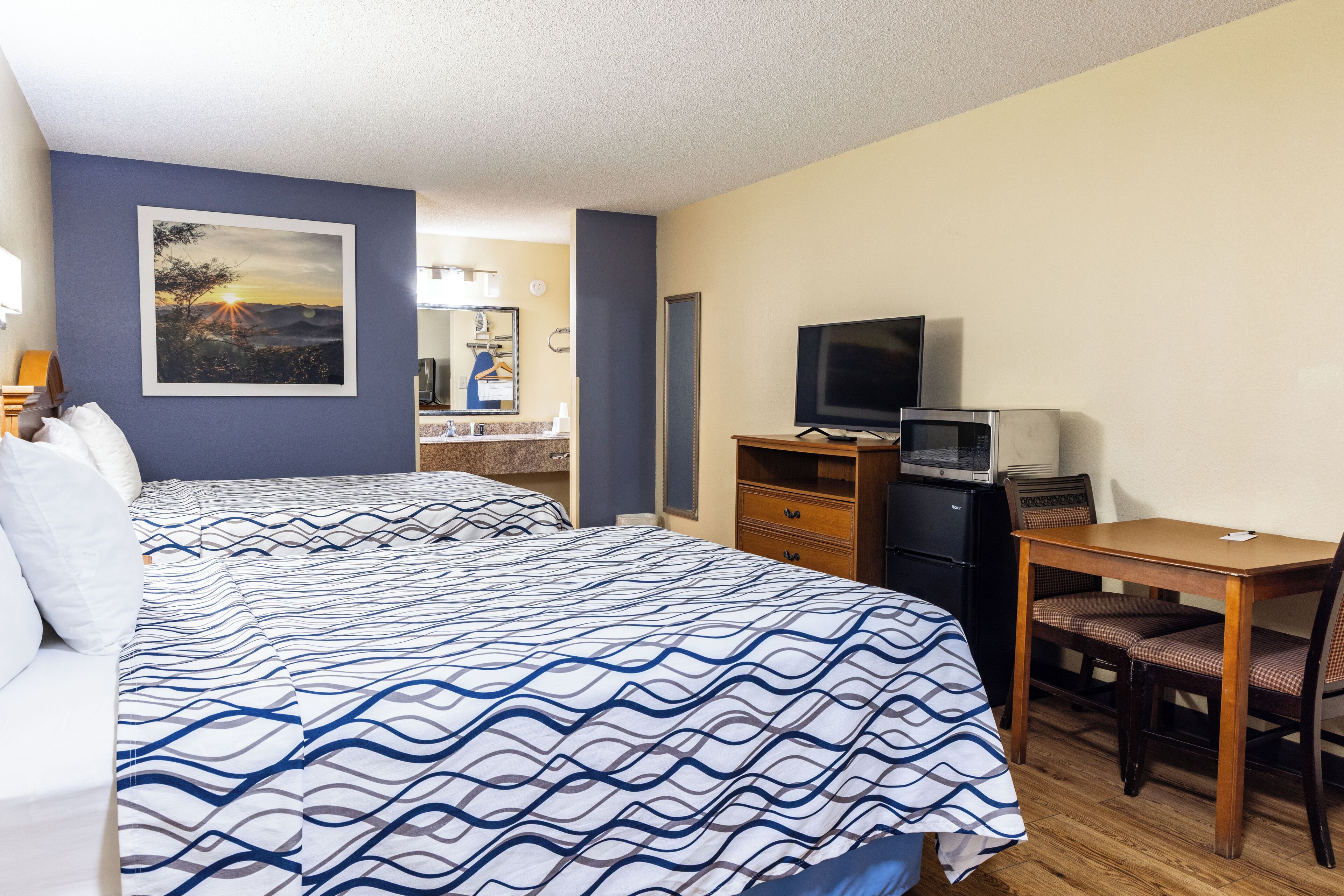 A hotel room with two beds, a desk with a chair, a television, and a microwave.