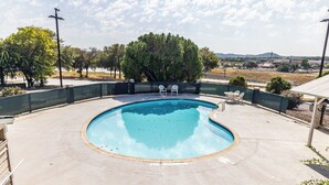 A round swimming pool with a green fence, two white chairs, and a view of trees and distant hills. - Boerne Inn and Suites (Boerne)