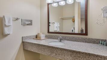 A bathroom with a granite countertop, a sink, a mirror with lights, and a towel rack.