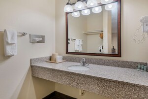 A bathroom with a granite countertop, a sink, a mirror with lights, and a towel rack.