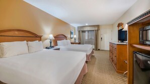 A hotel room with two beds, a TV, a refrigerator, and a desk with drawers.
