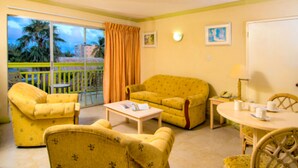 A room with yellow furniture, a balcony with orange curtains, and a view of palm trees. - Golden Sands Hotel (Oistins)