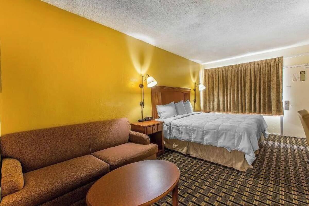 A hotel room with a bed, a sofa, a small table, and a nightstand.
