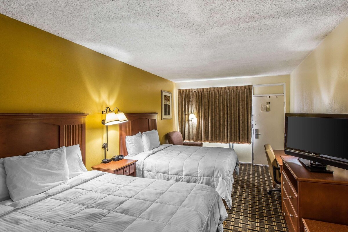 A hotel room with two beds, a television, a desk, and a window with curtains.