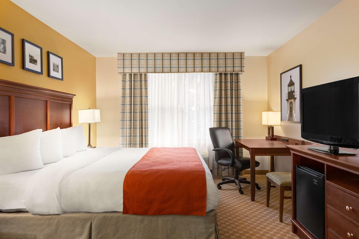 A hotel room with a bed, desk, chair, television, and a refrigerator.