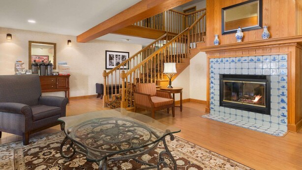 A spacious living room with a fireplace, a wooden staircase, and a glass coffee table. - Country Inn & Suites by Radisson, Holland, MI (Holland)