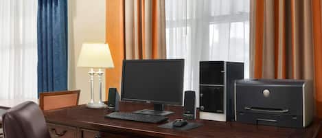 A hotel room with a wooden desk, two monitors, a printer, and a lamp.