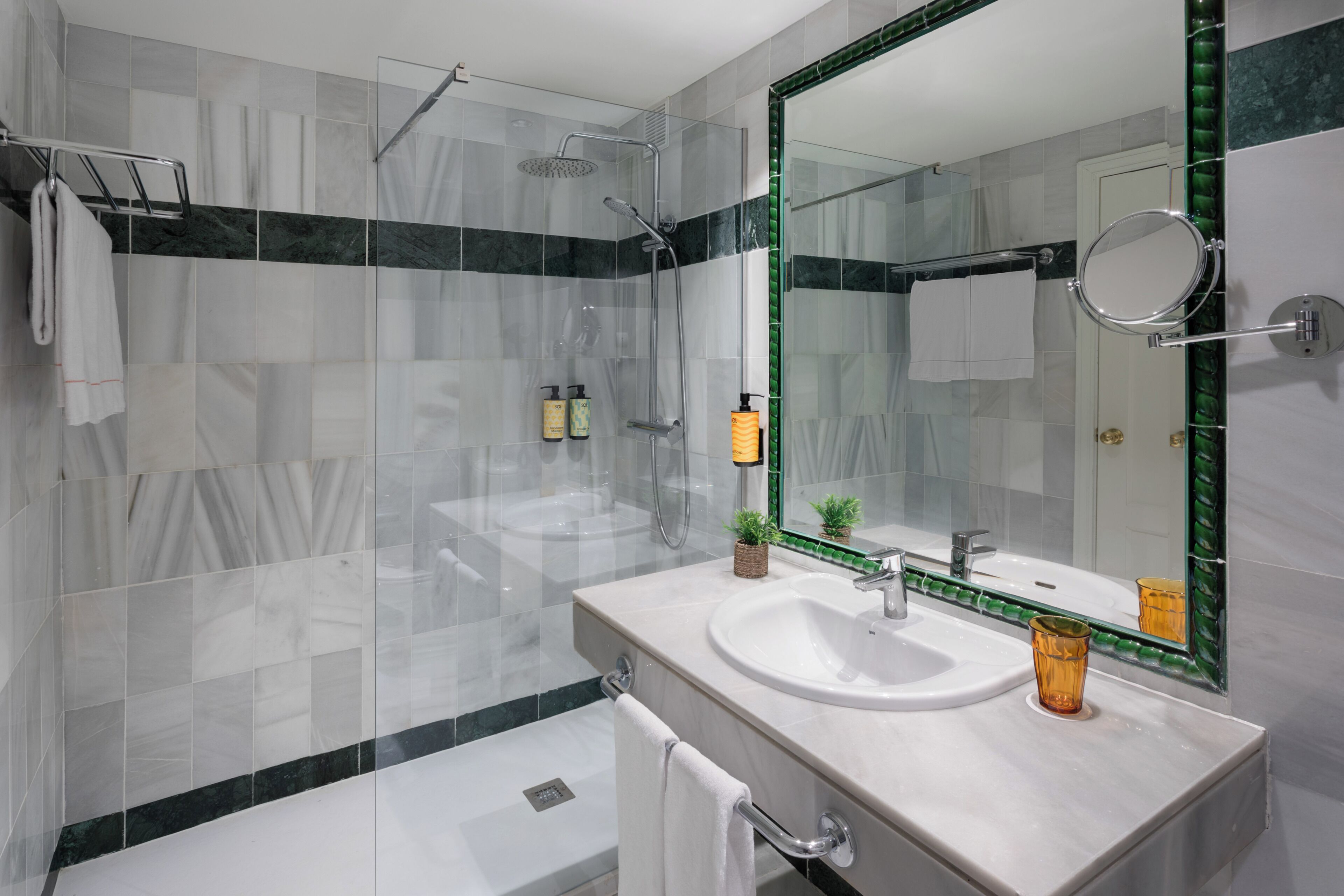 Une salle de bain moderne avec une douche à parois de verre, un lavabo blanc et un grand miroir doté d’un cadre vert.