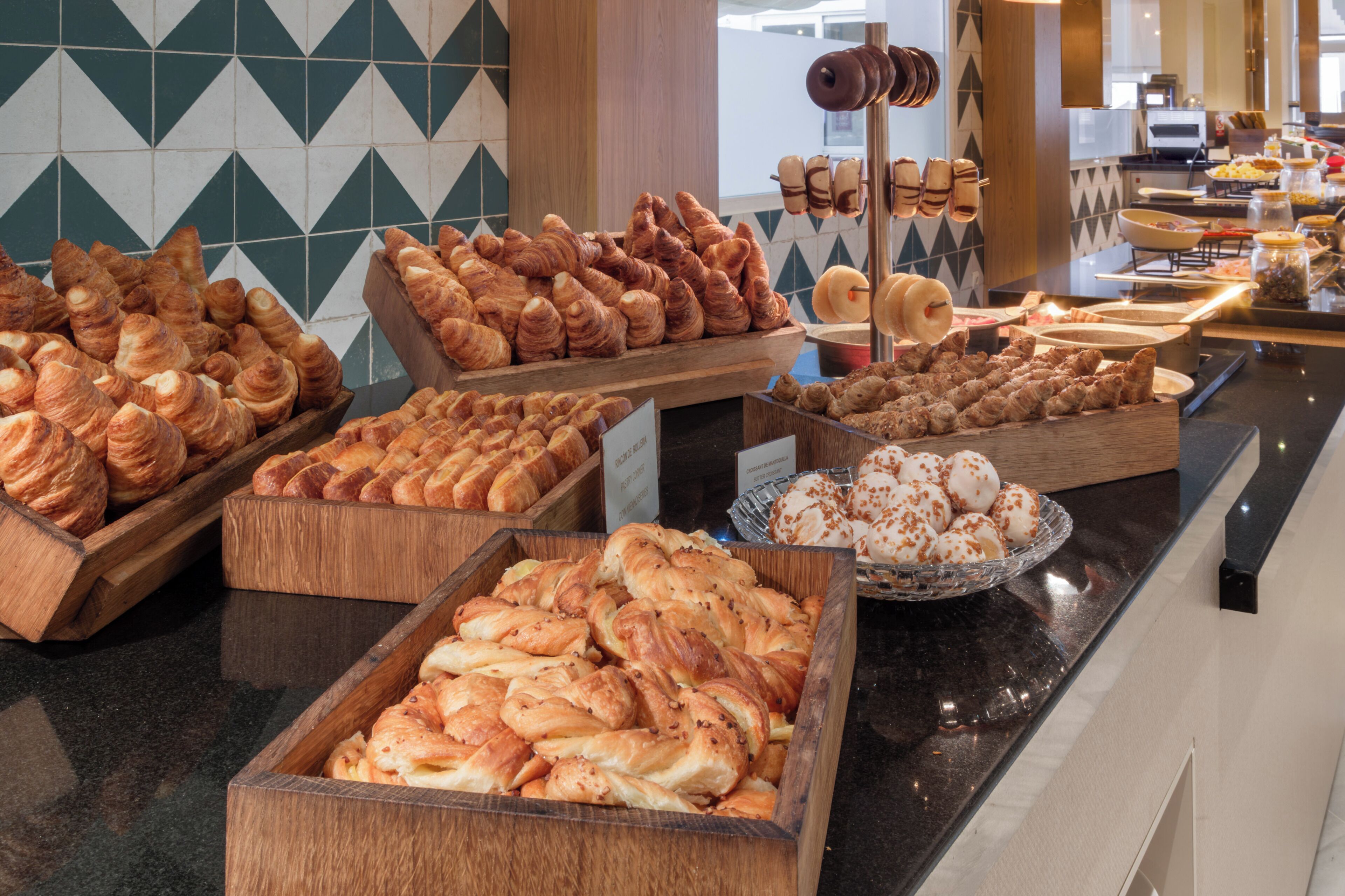 Diverse gebakjes gepresenteerd in houten kisten en een glazen schaal, met een keuken op de achtergrond.