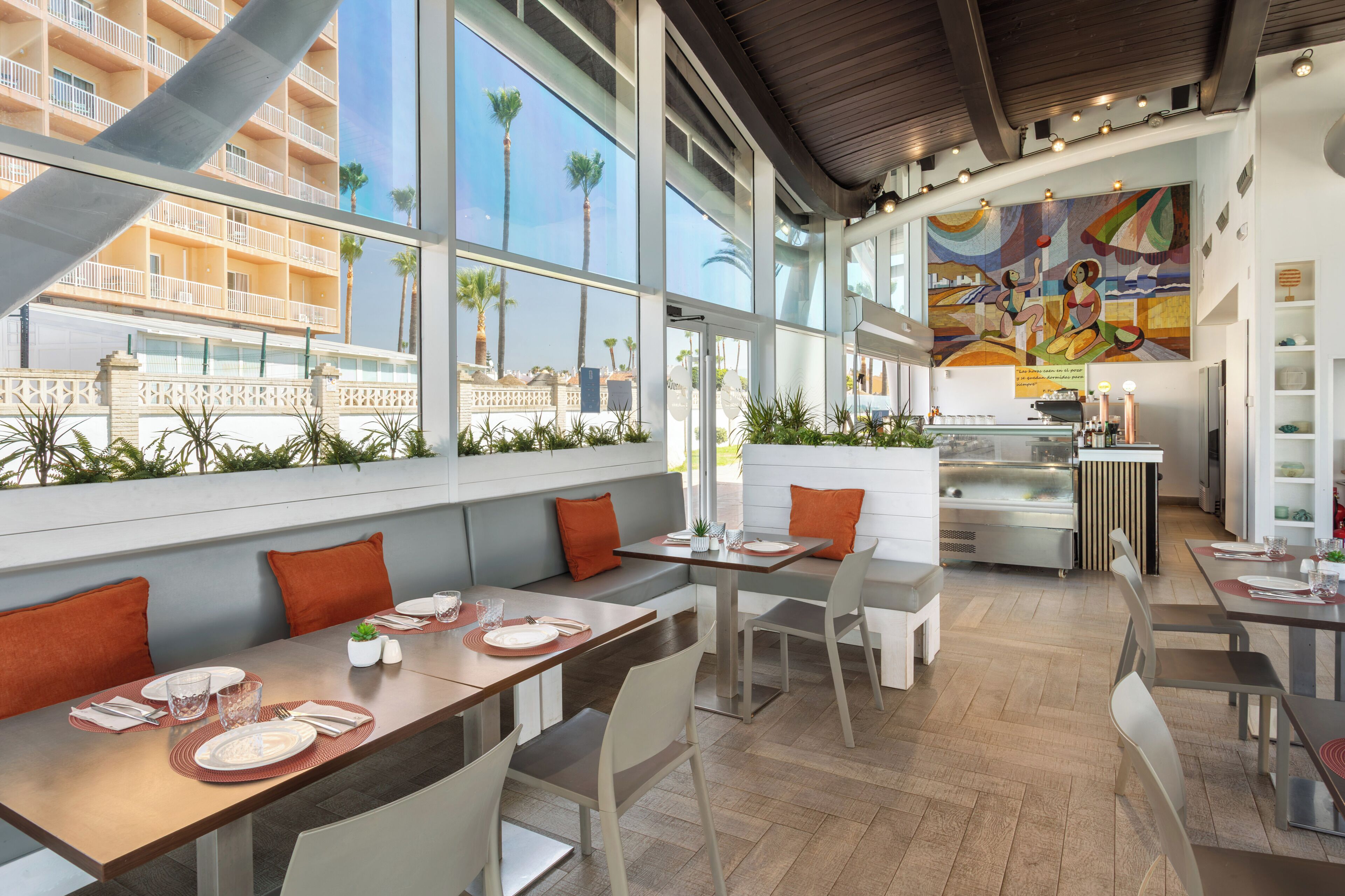 A modern dining area with high ceilings, large windows, and a view of a building with balconies.