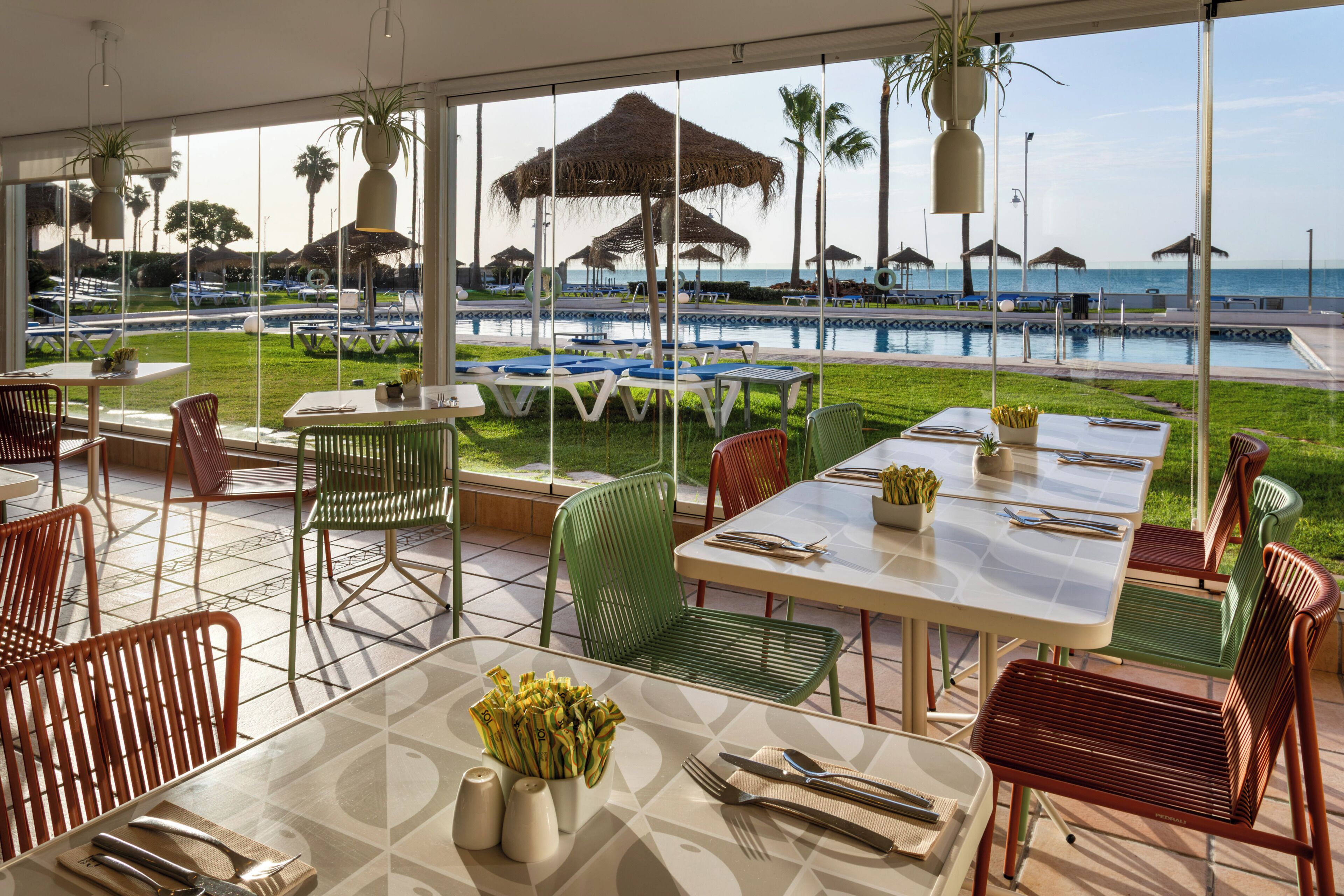 A restaurant with outdoor seating overlooking a pool and the sea.