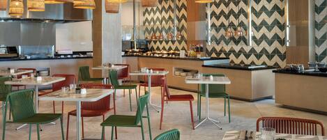 A restaurant with multiple dining tables and chairs, a bar area, and hanging pendant lights.