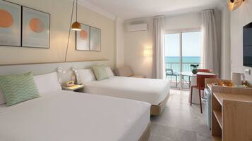 A hotel room with two beds, a desk with a chair, a TV, and a balcony with a view of the sea.