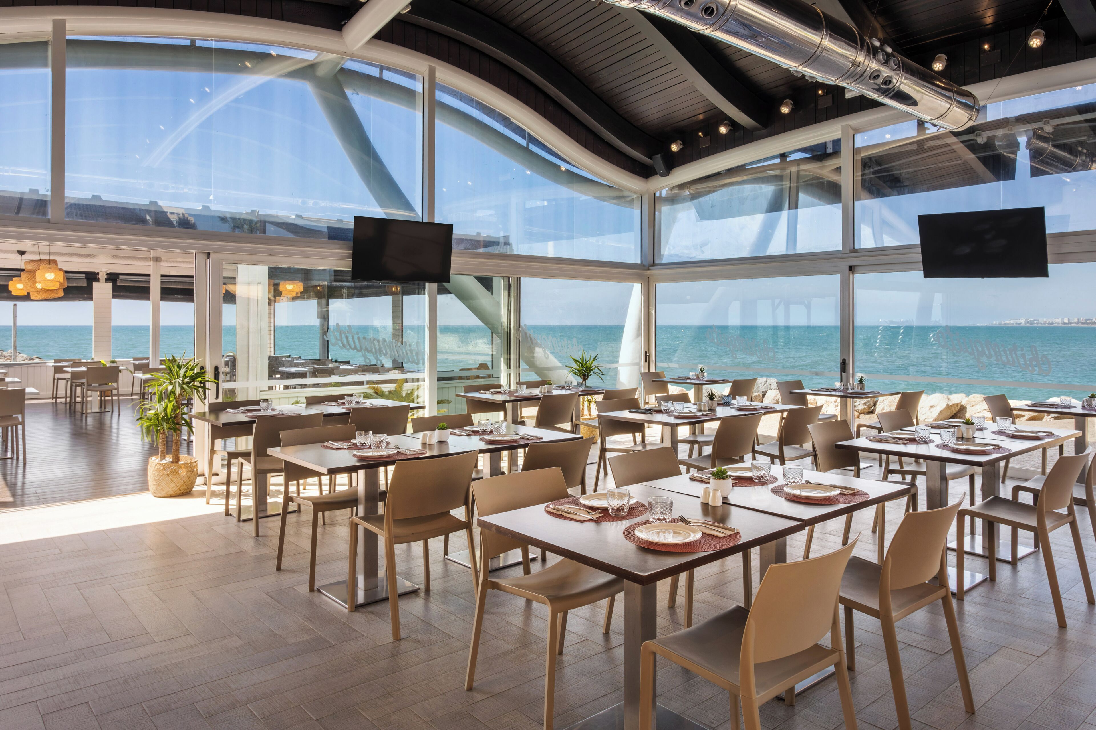 Een ruime eetruimte met tafels en stoelen, grote ramen en uitzicht op zee.